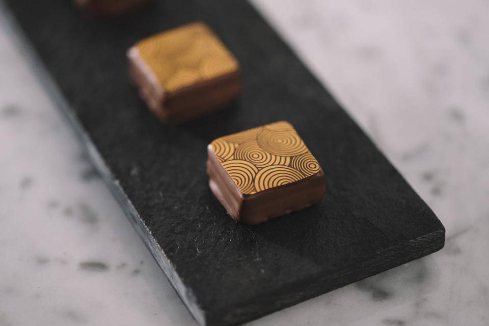 A black rectangular plate holding enrobed bonbons decorated with a spiral-patterned transfer sheet