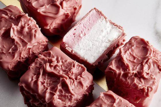 Two rows of marshmallows enrobed in Ruby chocolate, one is cut in half to reveal a pink and white layered interior