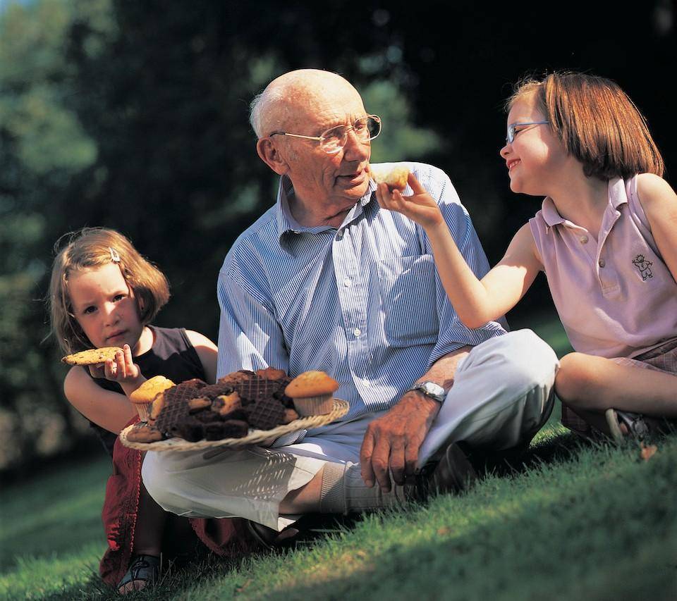 A grandfatherly gentleman shares chocolate treats a picnic with two young girls