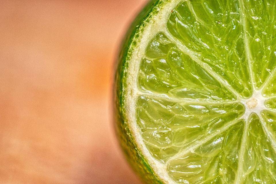 Horizontal image of lime slice on left, blurred reddish-brown background on right