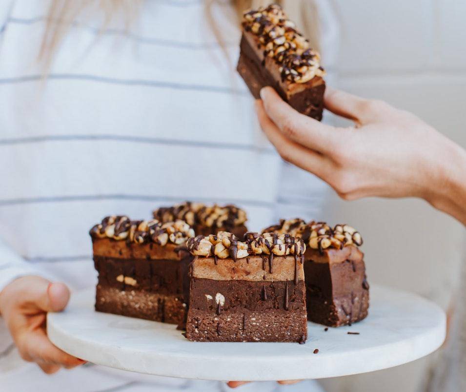 A woman holds a plate of tall, decadent layered brownies