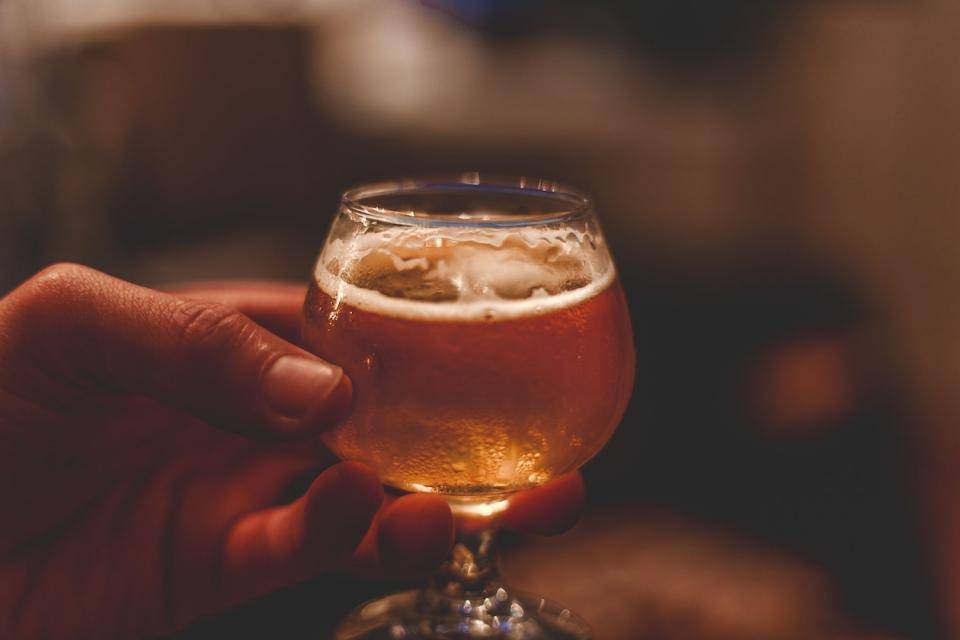 A hand holds a glass schooner of beer