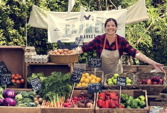 A smiling woman standing behind a display of produce at a farmer's market stall