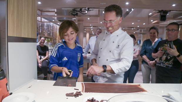 Ramon Morato makes chocolate curls assisted by a young cruise ship passenger
