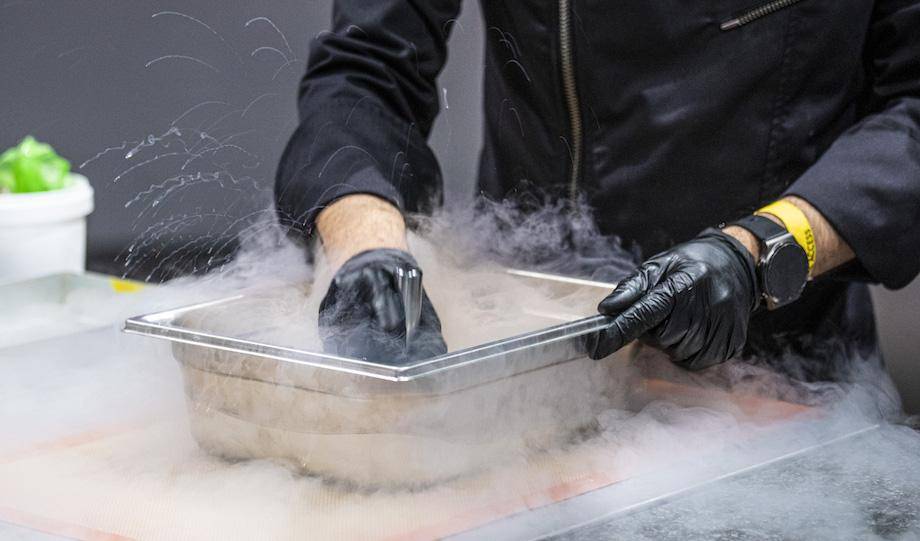 A chef's hands dipping a tool into a pan of dry ice