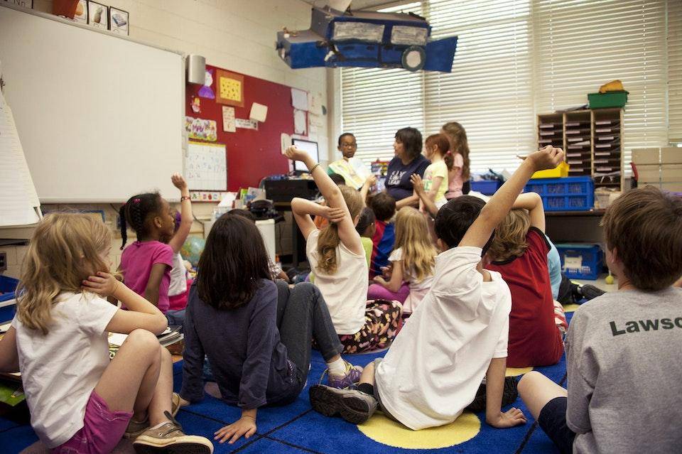 A classroom full of young children sitting on the floor while addressed by a teacher