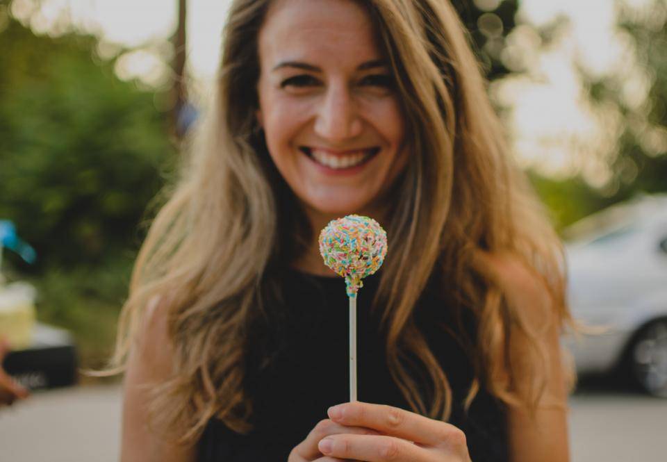 a woman smiles while holding a sprinkle-covered lollipop