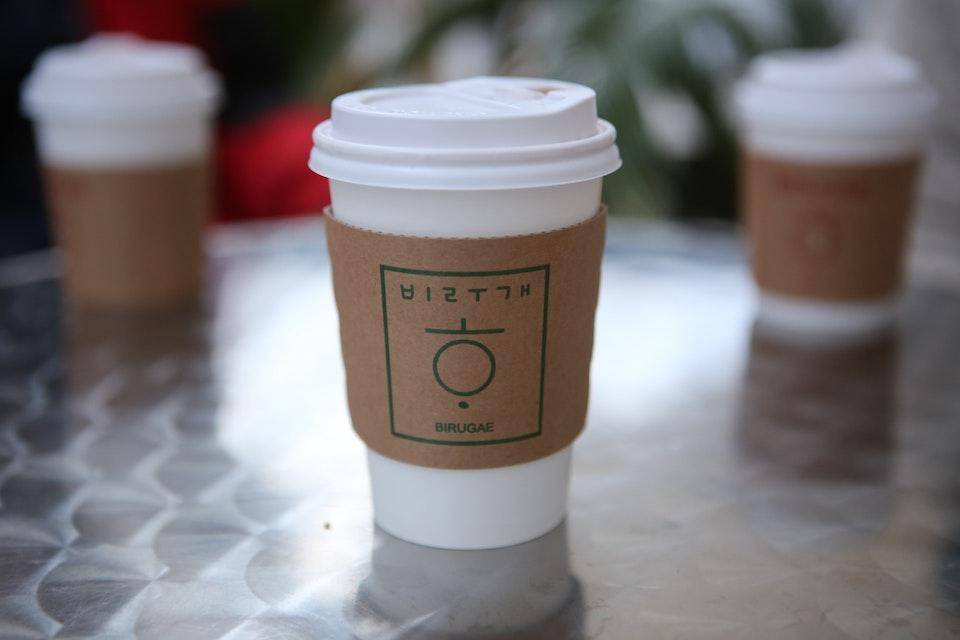 A paper coffee cup with a "cup cozy" made of undyed cardboard
