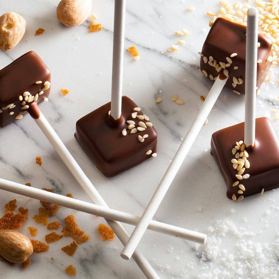 Square chocolate lollipops garnished with sesame seeds on a marble tabletop
