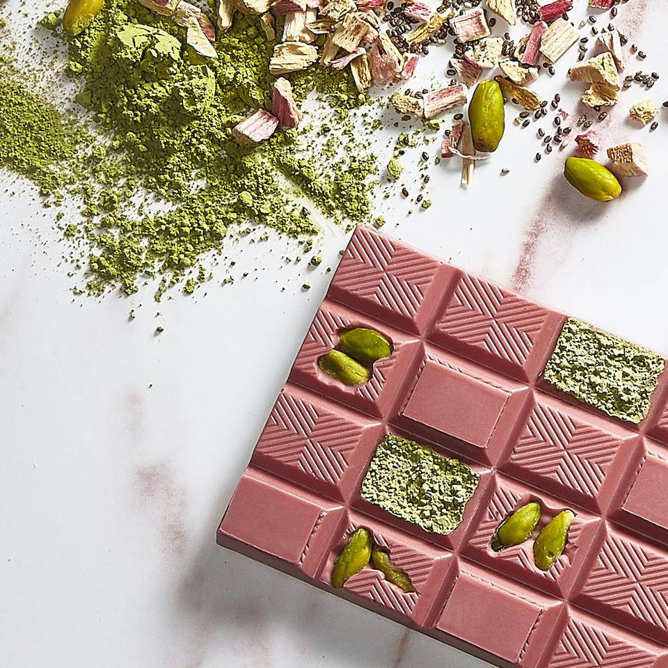 Ruby chocolate tablet with pistachio and green tea inclusions on a marble tabletop with green tea and chopped pistachios in background