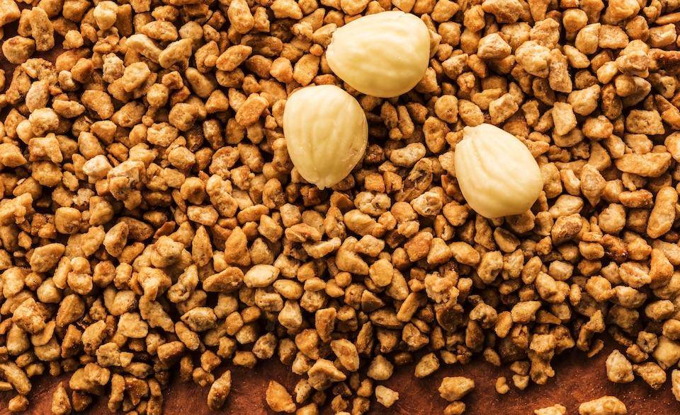 Three whole marcona almonds on a spilled pile of caramelized almond pieces