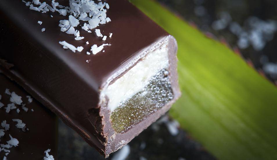 A rectangular bonbon cut open to reveal layers of coconut and pate de fruit, leaf in background