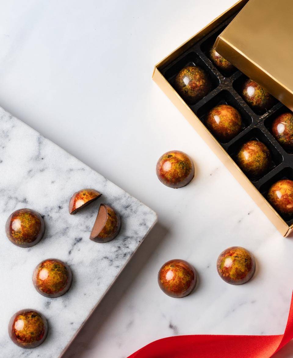 A partially open box of molded bonbons next to a marble slab holding bonbons, one of which is cut in half