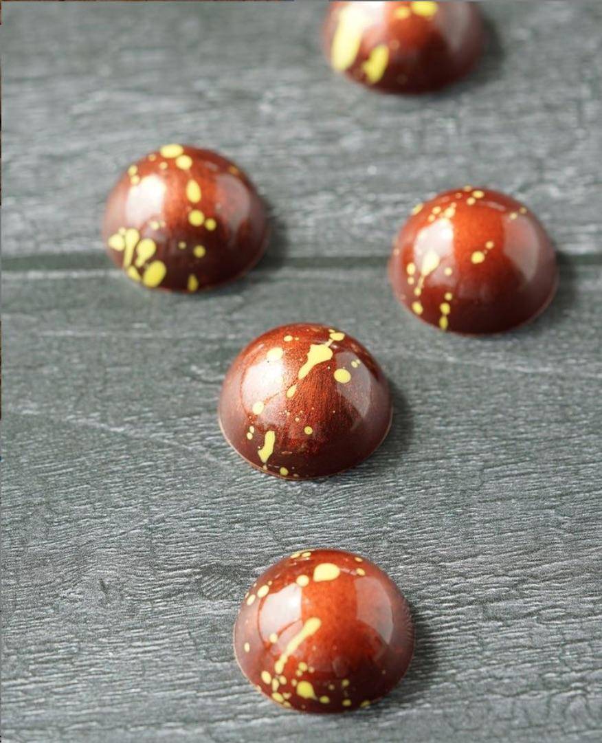 Half-sphere molded bonbons decorated with yellow cocoa butter splatter and copper luster dust