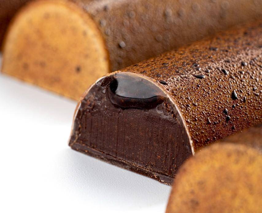 Close-up of a row of molded bars. One is cut to reveal a ganache and liquid center