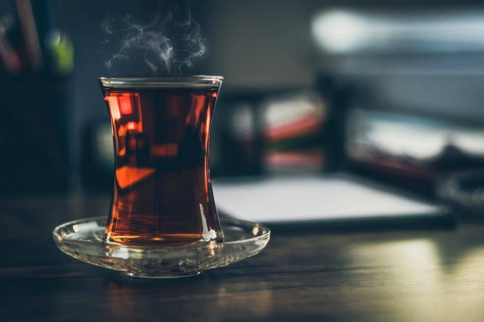 A steaming tall glass mug of tea on a table or desktop