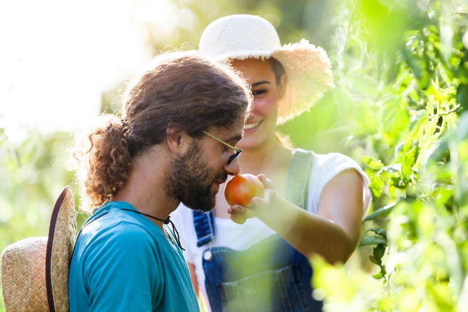Man in foreground smells fruit held out by woman in background