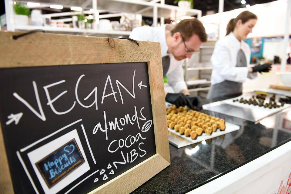 A food counter with chefs in the background. Prominent sign on counter reads: VEGAN