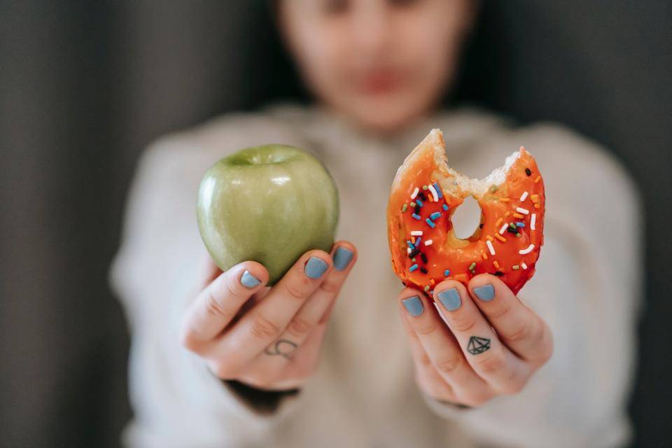 A person holds an apple and a donut outstretch toward the viewer. Choose your fighter.