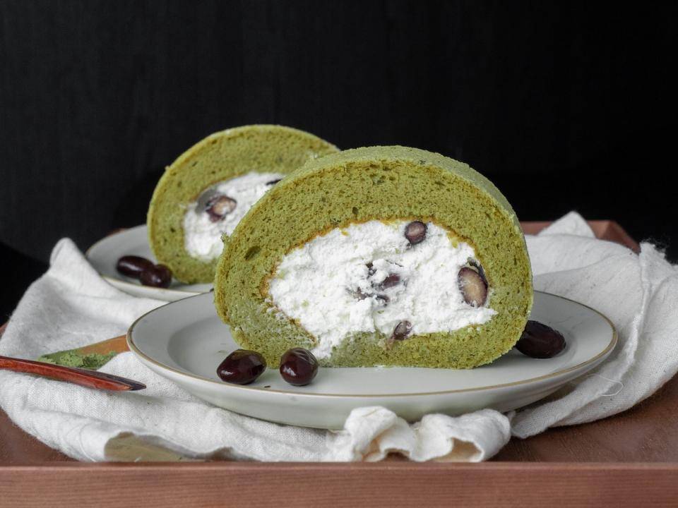 A slice of green jelly-roll-style cake filled with whipped cream and aduki beans