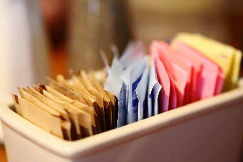 A sugar caddy with different colored packets of artificial sweeteners