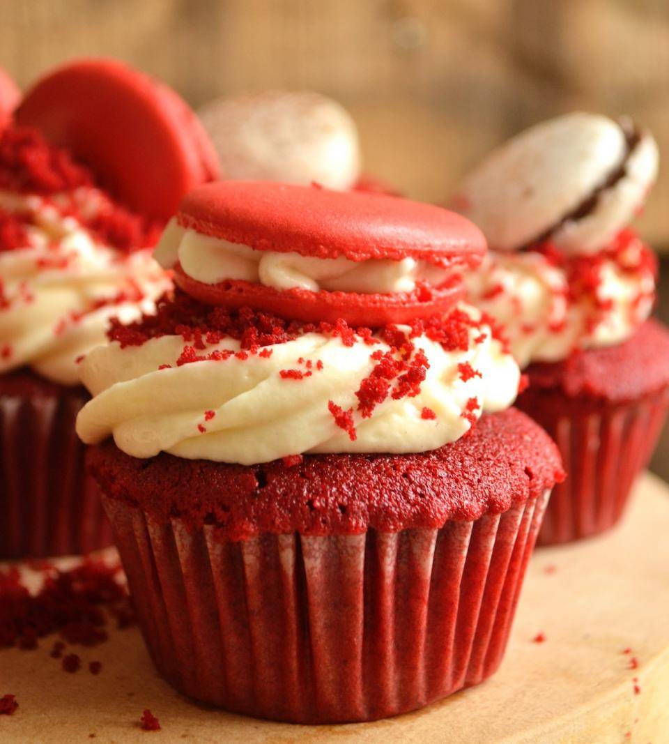 3 very, very red Red Velvet Cupcakes with a poof of icing on each and topped with a macaron