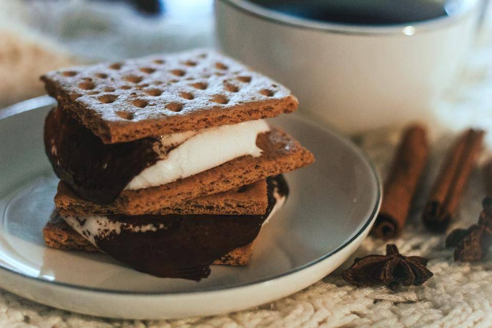 a stack of two S'mores graham sandwiches on a plate next to a mug of coffee
