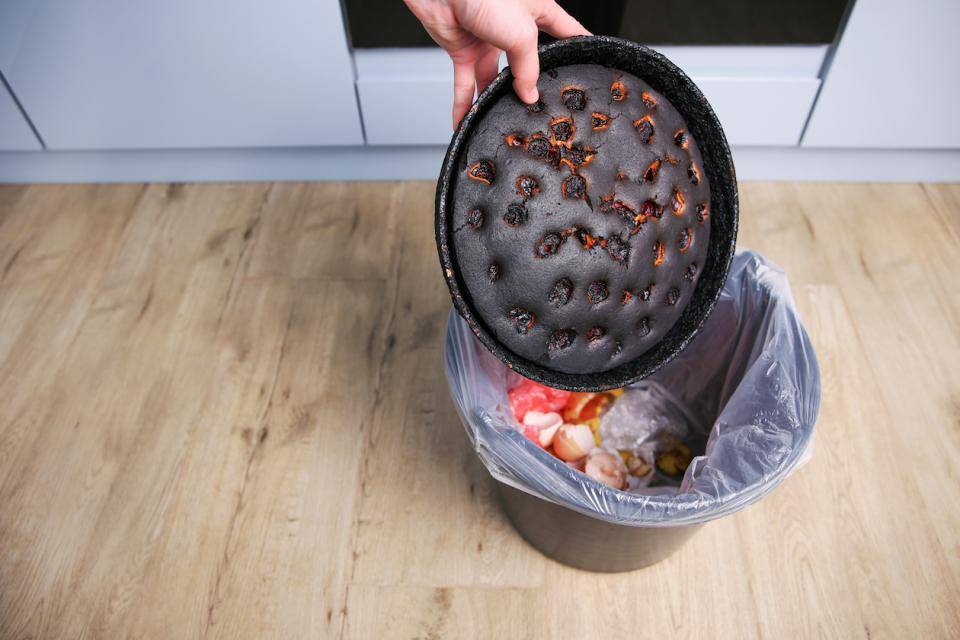 A hand drops a badly burnt pie into a trash can
