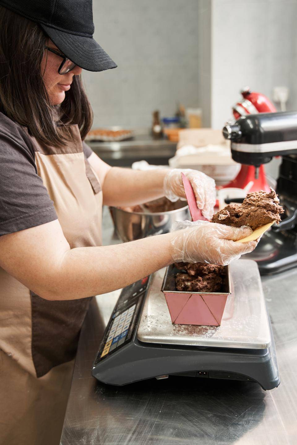 A baker weighs batter into a loaf pan set on a scale