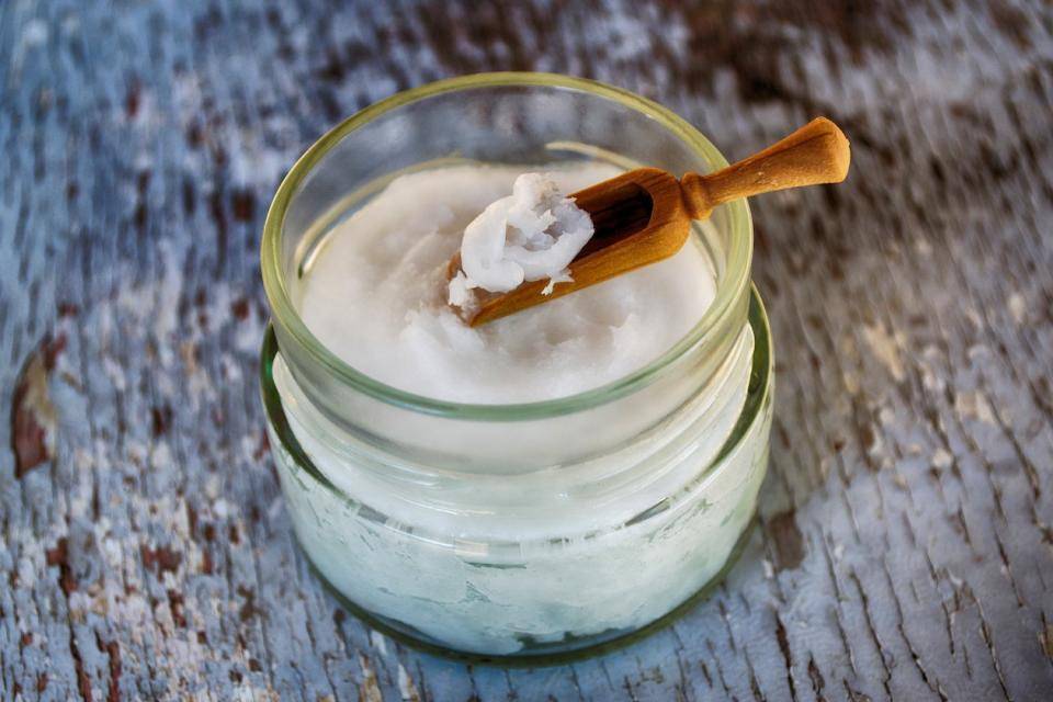 A jar of solid coconut oil with a small wooden spoon