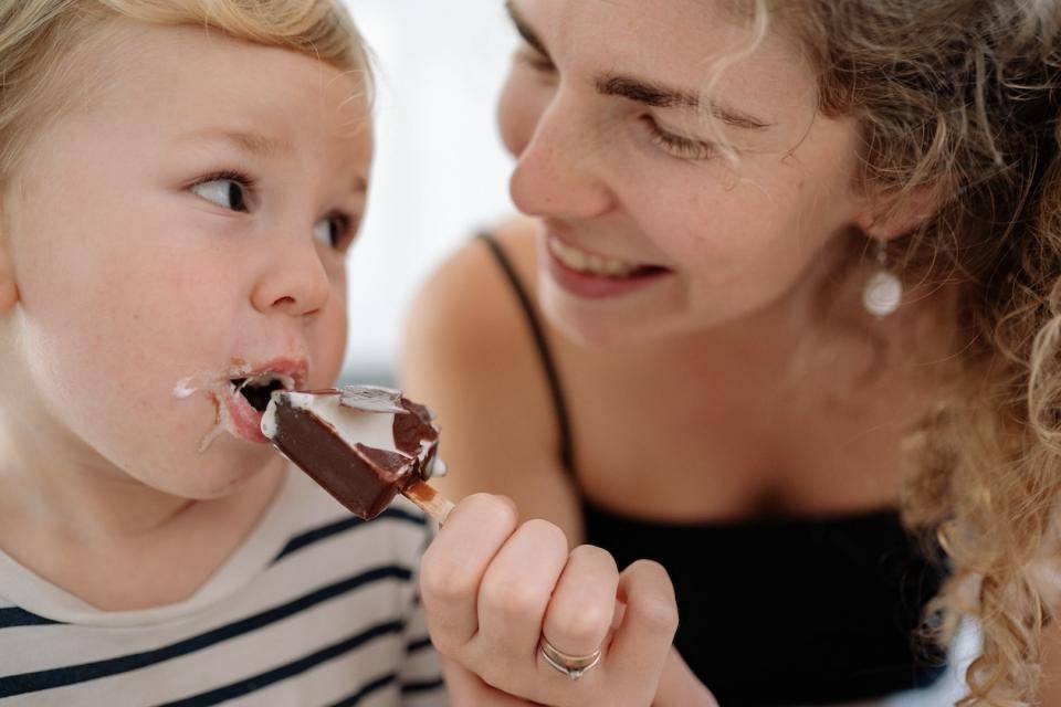 A mom and little boy share a chocolate-coated ice cream treat