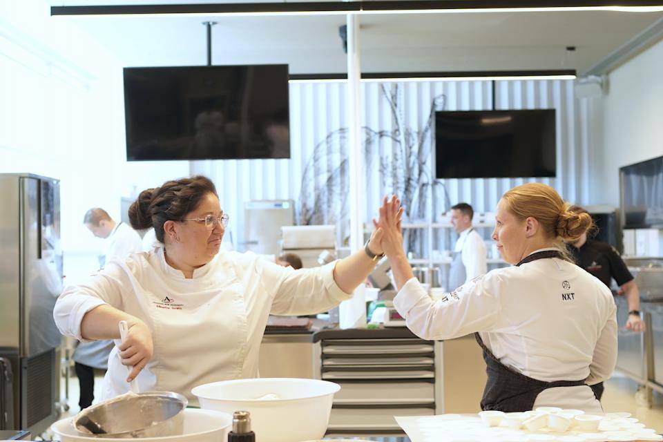 Chefs Minette Smith and Marike Van Beurden high-five during prep for the Chef Seminar