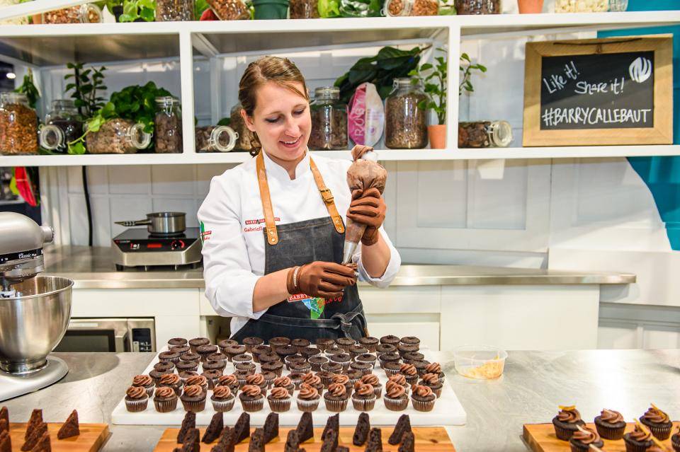 chef mulher recheando cupckaes de chocolate com chocolate, bancada com metade de cupckaes prontos e a outra a fazer