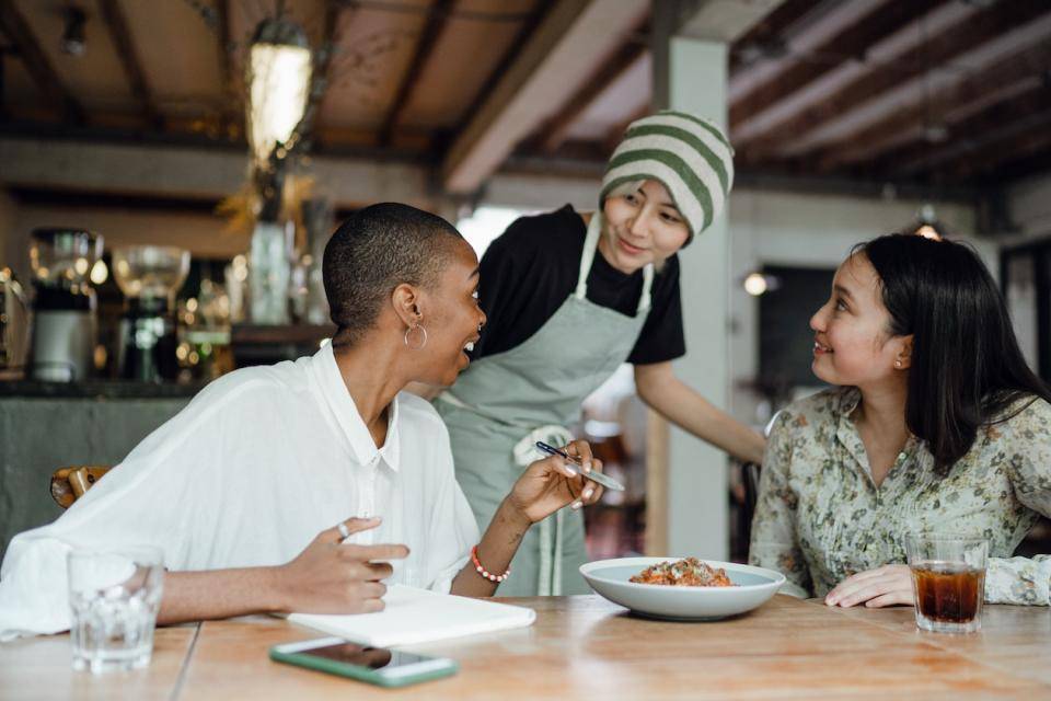 A server in a coffee shop talking to two guests at a table