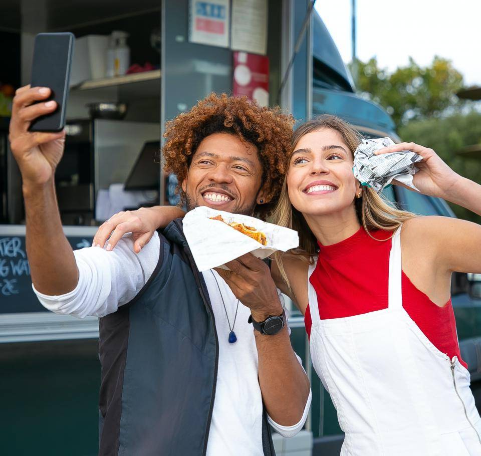 casal tirando selfie segurando um hamburguer