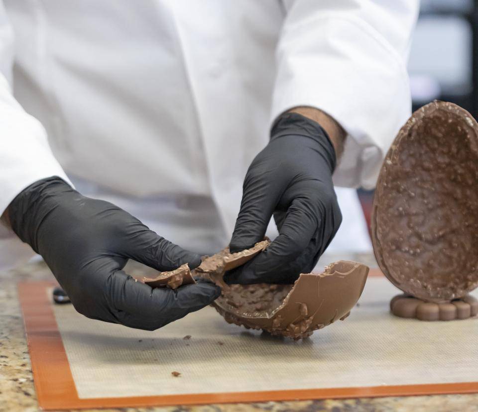 mão de chef com luvas pretas cortando ovo de chocolate com recheio na casca