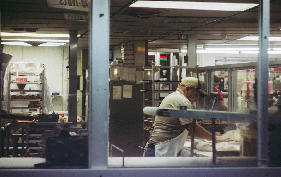 A man shapes dough in the work area of a small bakery