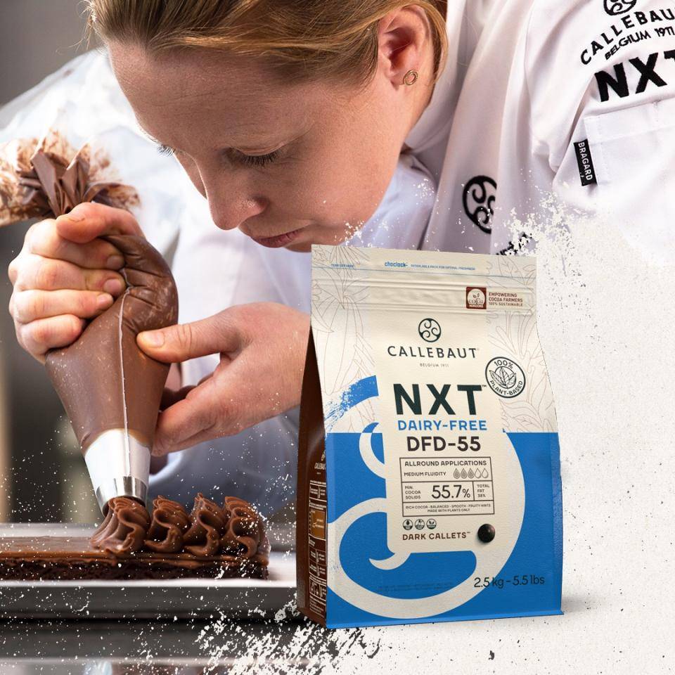 Chef Marike van Beurden pipes a dairy-free mousse made with Callebaut NXT onto a chocolate cake, bag of NXT plant-based chocolate in foreground