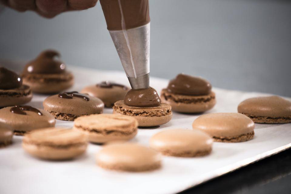 A chef pipes a plant-based creamy filling onto macaron shells