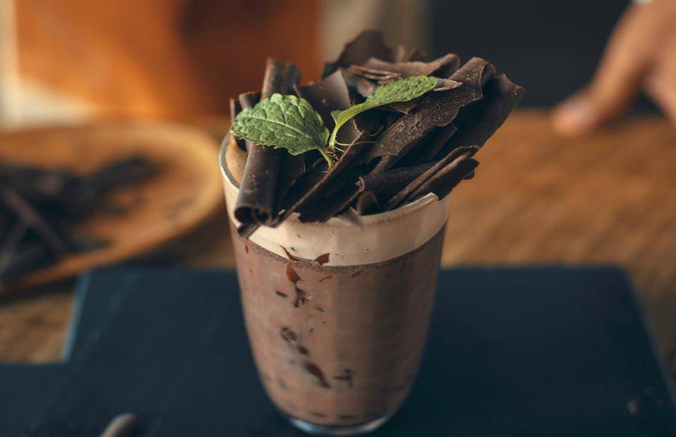 A decadent chocolate beverage topped with large chocolate shavings and fresh mint