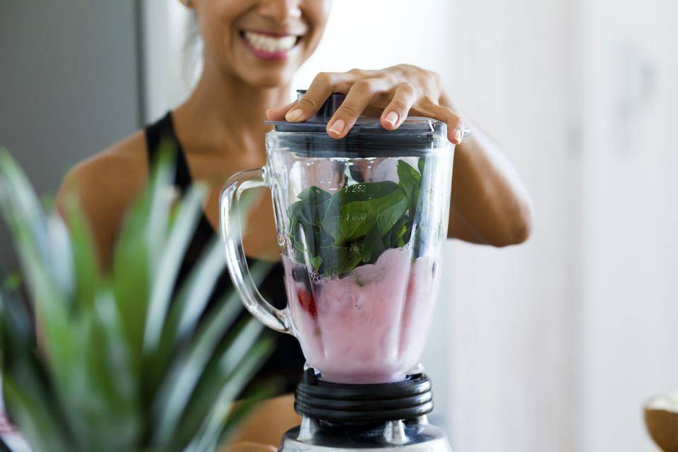 A smiling woman blends a healthy smoothie with spinach, berries, and yogurt