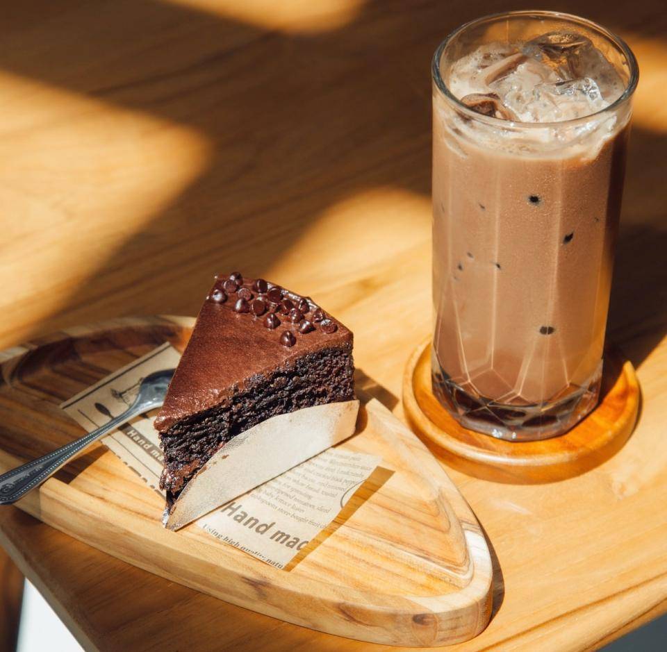 A small wedge of chocolate cake paired with a cold chocolate drink