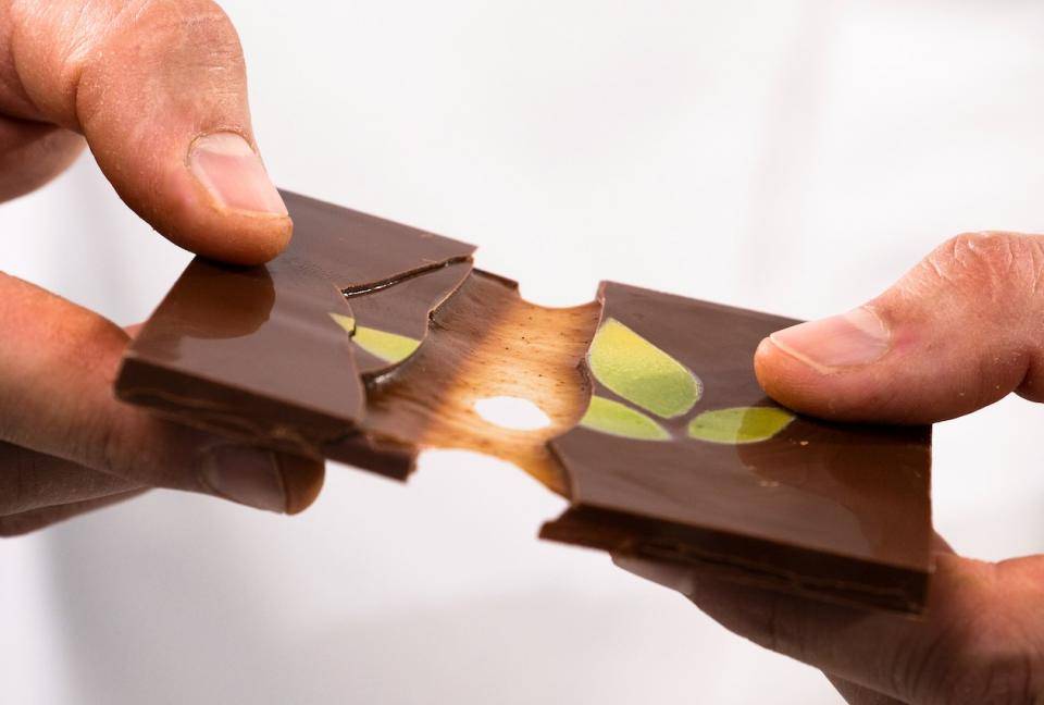 A chocolate tablet being broken in half to reveal a gooey caramel layer