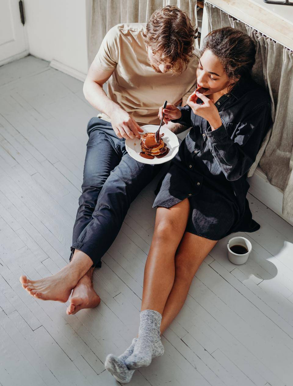 duas pessoas sentadas no chão encostadas em uma bancada comendo panquecas com chocolate