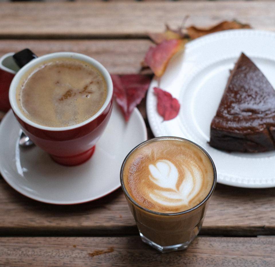 foto tirada de cima de uma mesa com um prato e uma torta de chocolate, um copo de café e um copo de chocolate