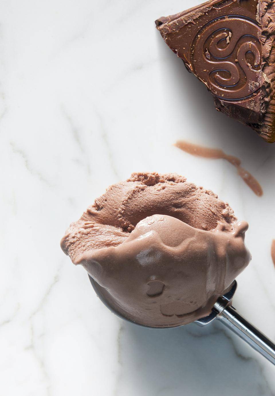 A scoop of chocolate gelato with a brick of dark chocolate in the background