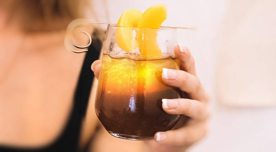 a woman holding a glass containing a coffee shandy: coffee on the bottom, lemonade on top