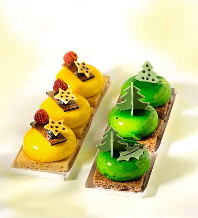 Individual Mousse desserts colored bright yellow and green and topped with chocolate decor