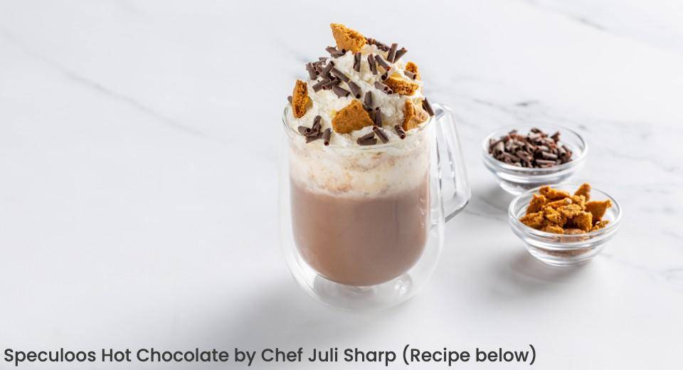 A mug of hot chooclate toppped with whipped cream, crispearls and cookie pieces