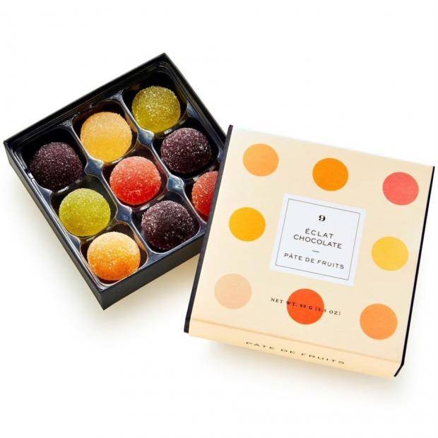 An open box of half-sphere shaped fruit jellies, the lid has a polka-dot print and is leaning, face-up, on the bottom of the box
